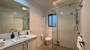 Uma casa de banho moderna com cabine de duche em vidro, um espelho grande, uma sanita e lavatório com bancada de mármore.