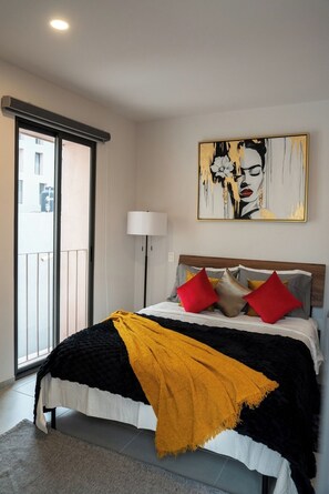 Ein Schlafzimmer mit Bett, Fenster, Stehlampe und einem Gemälde an der Wand.