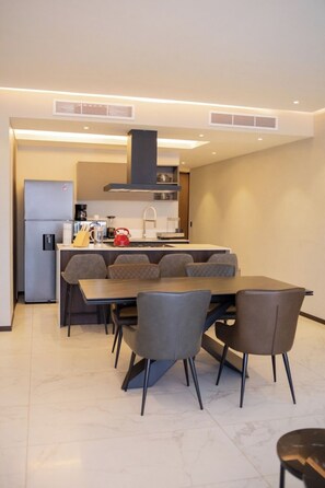 A modern kitchen with a dining area, including a large table and chairs, a refrigerator, and a coffee maker.