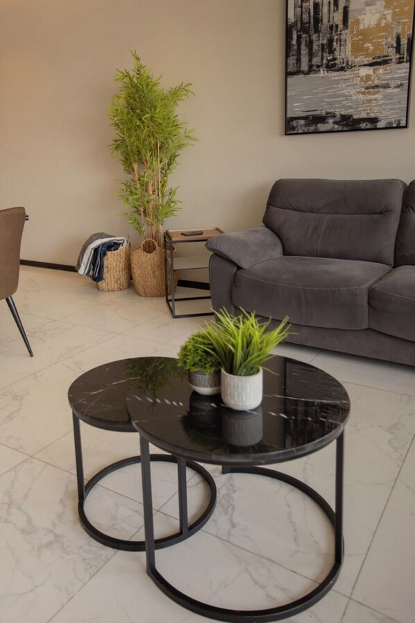 A modern living room with a grey sofa, a round black table with two potted plants, a large painting on the wall, and a plant in a woven basket. - Mr. W : Exceptional apartment 2BR Cauda (Guadalajara)