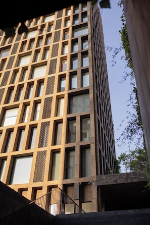 Um edifício de vários andares com fachada em forma de grade, grandes janelas e uma escadaria visível que leva à entrada.