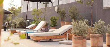 A rooftop pool area with lounge chairs, potted plants, and a staircase leading up.