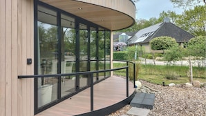 Ein modernes Gebäude mit großen Glasfenstern, einer geschwungenen Holzdielen-Terrasse und einem Metallgeländer.