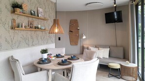 Ein Essbereich mit rundem Tisch, Stühlen und einem an der Wand befestigten Fernseher.