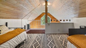 Une chambre avec un plafond en pente, un lit surmonté d’un tapis à motifs, un bureau et une vue sur l’extérieur.