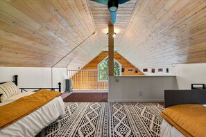 A bedroom with a sloped ceiling, a bed with a patterned rug, a desk, and a view of the outdoors. - Olympic Peninsula Base Camp | Lake Cushman (Hoodsport)