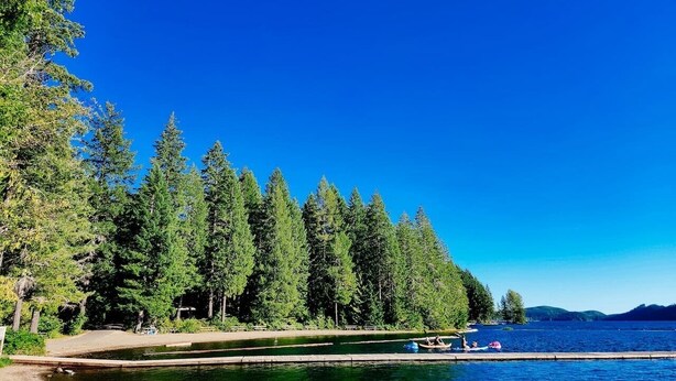 Une vue sur le lac, avec des arbres denses, un ciel dégagé et un quai où sont amarrés des bateaux.