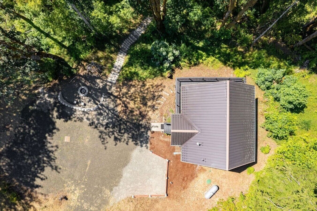 An aerial view of a house with a sloped roof, a paved driveway, and a small yard with a circular structure.