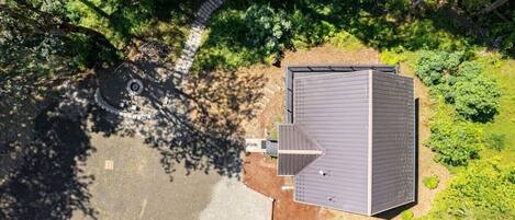 An aerial view of a house with a sloped roof, a paved driveway, and a small yard with a circular structure.