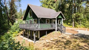 Une maison verte avec un balcon, entourée d’arbres.