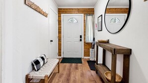 Un couloir avec un banc en bois, un miroir, une porte dotée d’un panneau de verre et une petite table sur laquelle se trouve un panier.