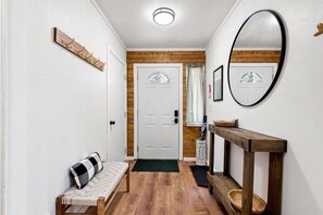 A hallway with a wooden bench, a mirror, a door with a glass panel, and a small table with a basket. - Olympic Peninsula Base Camp | Lake Cushman (Hoodsport)