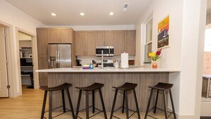 Une cuisine moderne avec des meubles en bois, des appareils en acier inoxydable et un coin bar équipé de tabourets.