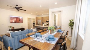 Un coin repas avec une table en bois dressée pour quatre personnes, un canapé bleu et une cuisine en arrière-plan.