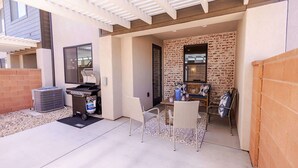 Une terrasse extérieure avec un barbecue, un espace salon et un mur en briques.