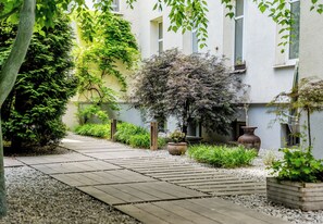 A pathway leading to a building with a garden area, including a small tree and potted plants. - Kopernika Old Town Apartment (Poznań)