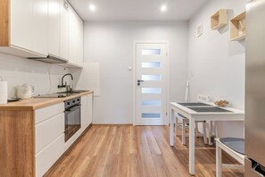 A compact kitchen with white cabinets, a wooden countertop, a stove, and a table with chairs. - Chorzów Charming Apartment (Chorzów)