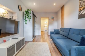 Un salon moderne avec un canapé bleu, un téléviseur, une plante et un plancher en bois.
