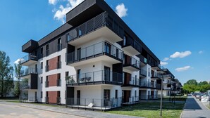 A multi-story residential building with balconies, a paved driveway, and a clear sky.