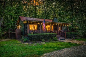 Uma cabana rústica com varanda, uma bandeira americana e um jardim bem cuidado.