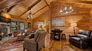 A cozy log cabin interior with a fireplace, leather furniture, and a dining area. - Creekside Green - Firepit | Gazebo alongside creek | pond (Cherry Log)