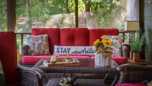 A cozy seating area with a sofa, cushions, and a sign that reads 'STAY awhile'. - Creekside Green - Firepit | Gazebo alongside creek | pond (Cherry Log)