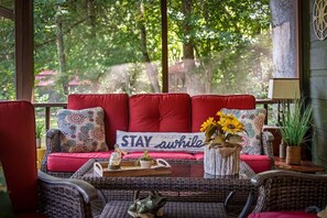 Um espaço de estar aconchegante com sofá, almofadas e uma placa com a inscrição 'STAY awhile'.