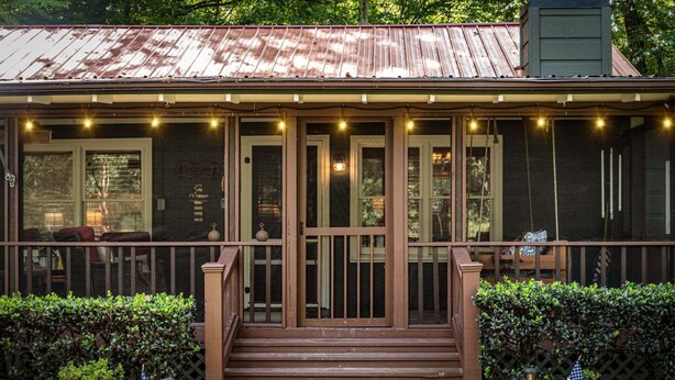 A house with a porch, steps, and a railing. There are two American flags on the ground. - Creekside Green - Firepit | Gazebo alongside creek | pond (Cherry Log)