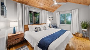 A bedroom with a wooden ceiling, a bed with white and blue bedding, a nightstand with a lamp, a chair, and a potted plant. - Blue Moon Rise - Pet Friendly | Mountain View | Hot Tub (Blue Ridge)