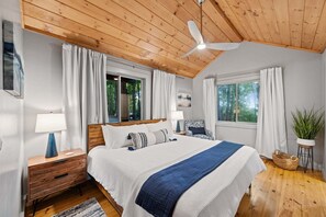 A bedroom with a wooden ceiling, a bed with white and blue bedding, a nightstand with a lamp, a chair, and a potted plant. - Blue Moon Rise - Pet Friendly | Mountain View | Hot Tub (Blue Ridge)