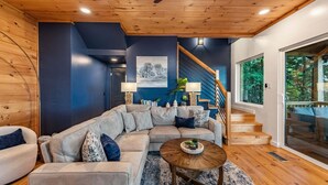 A modern living room with a sectional sofa, a coffee table, and a staircase leading to a balcony. - Blue Moon Rise - Pet Friendly | Mountain View | Hot Tub (Blue Ridge)