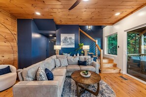 A modern living room with a sectional sofa, a coffee table, and a staircase leading to a balcony. - Blue Moon Rise - Pet Friendly | Mountain View | Hot Tub (Blue Ridge)