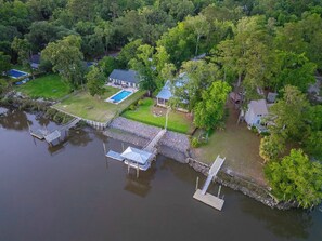 Eine Luftaufnahme eines Sees mit einem Anwesen, das einen Steg, ein Schwimmbad und ein von dichten Bäumen umgebenes Haus umfasst.