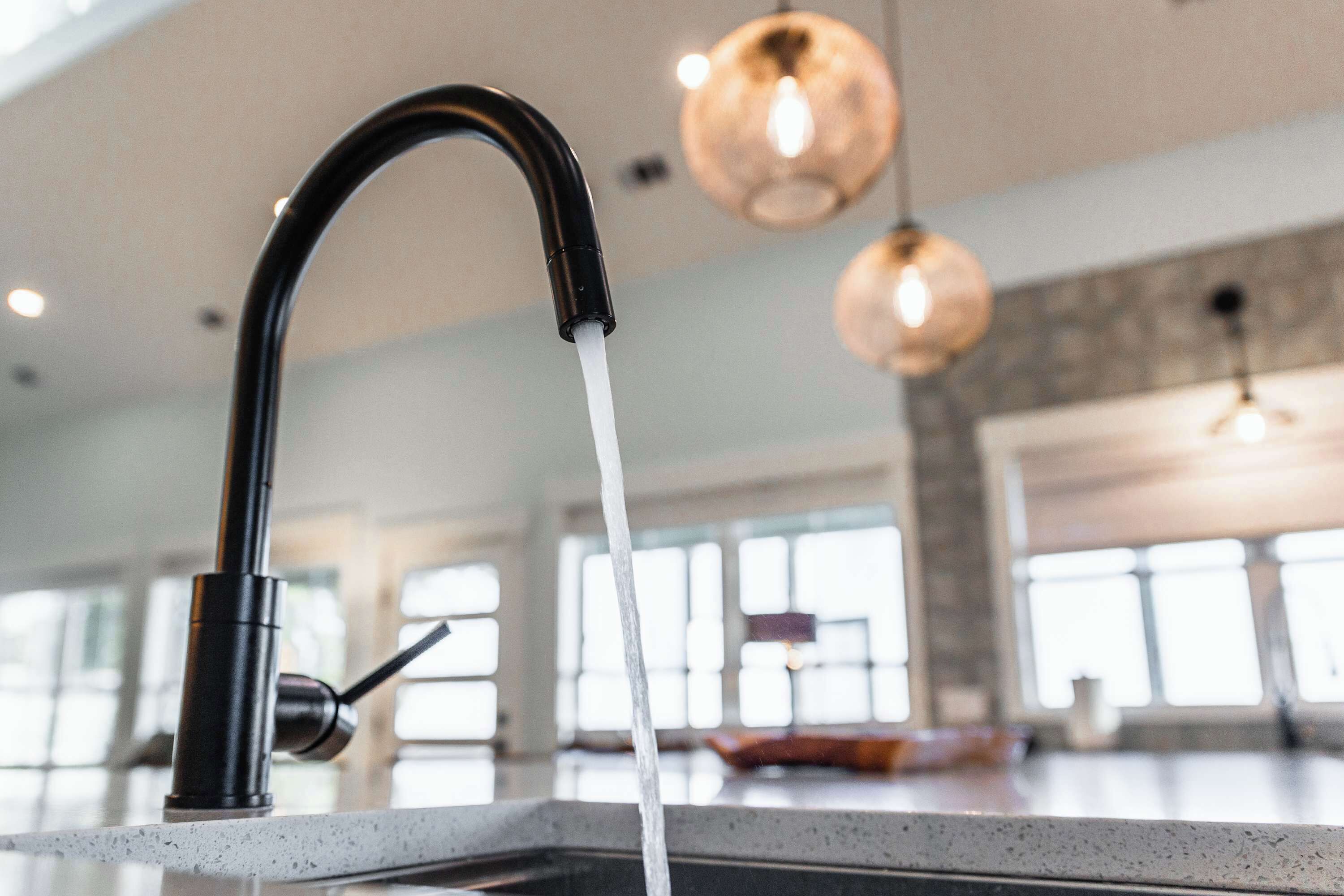 Une cuisine dotée d’un robinet moderne, de grandes fenêtres et de luminaires suspendus.