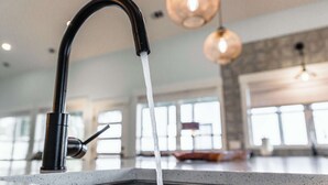 A kitchen with a modern faucet, large windows, and pendant lighting.
