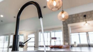 Une cuisine dotée d’un robinet moderne, de grandes fenêtres et de luminaires suspendus.