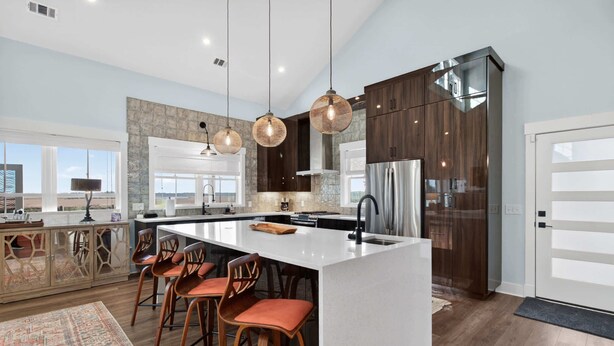 A modern kitchen with a large island, bar stools, pendant lighting, and a view of the landscape.