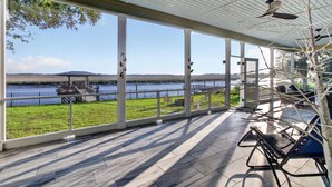 A covered patio with a view of a lake, outdoor seating, and a fan.