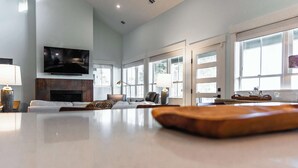 A spacious living area with a fireplace, comfortable seating, a flat-screen TV, and large windows.