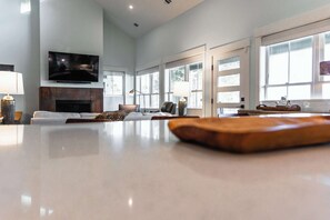Un salón amplio con chimenea, asientos cómodos, un televisor de pantalla plana y ventanas grandes.