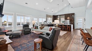 A spacious living area with a high ceiling, large windows, a kitchen, and a dining area.