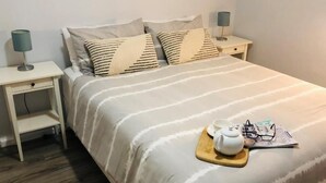 A neatly made bed with a tray of tea set, a magazine, and glasses on the bed. There are two bedside tables with lamps. - Apiwa Middleton Beach Front Apartments Albany  (Middleton Beach)