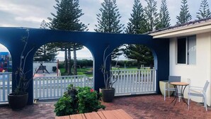 A patio area with a wooden table and chairs, a blue archway, and potted plants. - Apiwa Middleton Beach Front Apartments Albany  (Middleton Beach)