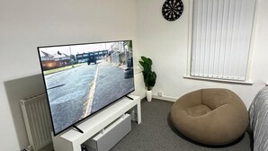 A living room with a flat-screen TV, a white radiator, a potted plant, a bean bag, and a dartboard. - Kensington Studio, 2nd-Floor City Base (Kensington)