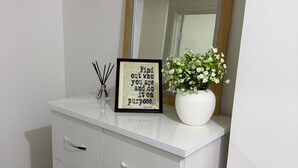 A white dresser with a mirror, a framed inspirational quote, and a vase with white flowers. - Kensington Studio, 2nd-Floor City Base (Kensington)
