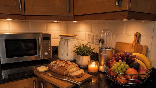 Eine Küche mit Mikrowelle, Brot, Obstschale, Kerze und Mixer.