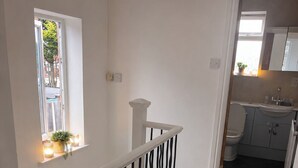 Eine Treppe mit weißer Geländer, ein kleines Fenster mit einer Pflanze und Blick in einen Küchenbereich.