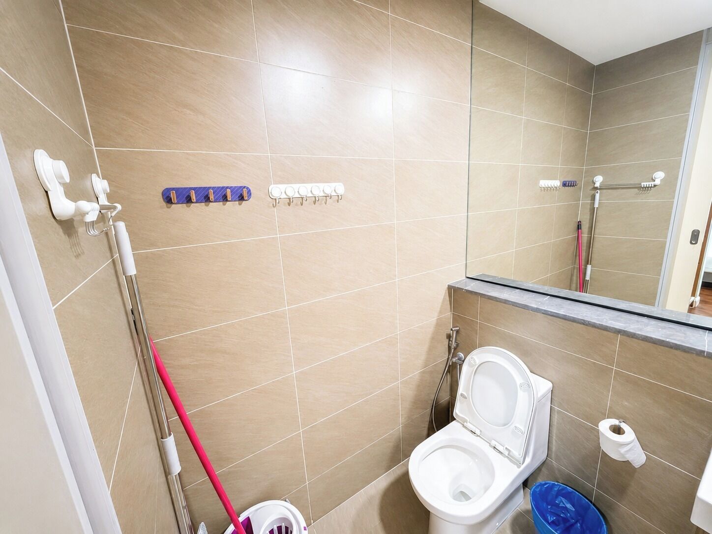 A bathroom with a toilet, bidet, hand dryer, and a blue trash bin.