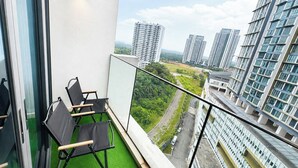 Un balcón con vista a edificios altos, suelo de césped artificial verde y dos sillas plegables negras.
