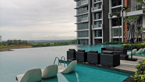 Una piscina moderna de hotel con vista al océano, rodeada de sillones de descanso y un edificio de gran altura.
